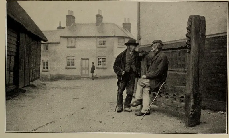 Old photograph of two elderly men in hats beside the wooden stocks and whipping post in the Bury, Odiham