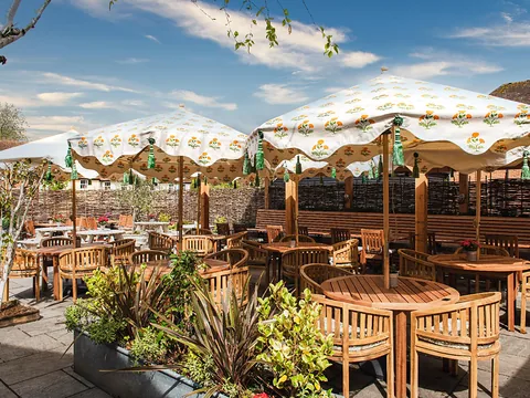 The sunny garden at Bel & the Dragon in Odiham, with wooden tables and chairs under patterned parasols