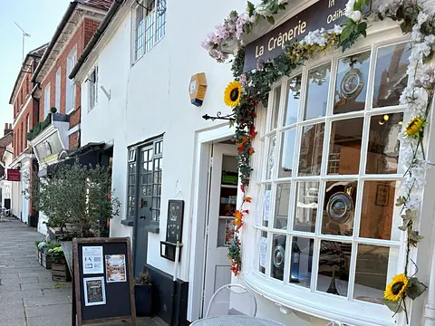 The front of La Crêperie on Odiham High Street, a white-painted shop with a flower-garlanded sign and a bay window