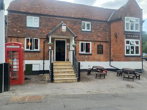The front of the Fox & Goose in Greywell, a red-brick pub with steps up to the door, a red phone box and picnic benches outside