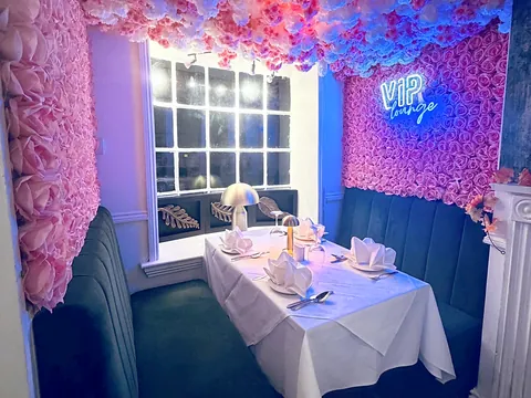 A cosy booth at Odiham Tandoori with a wall of pink flowers, a neon sign and a table laid for dinner