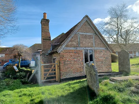 Odiham's Pest House, a small 17th-century brick cottage with a tiled roof in the corner of the churchyard