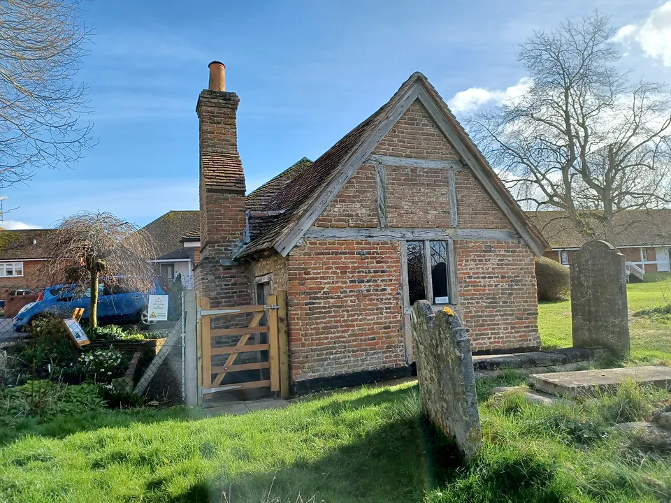 Odiham's Pest House, a small 17th-century brick cottage with a tiled roof in the corner of the churchyard